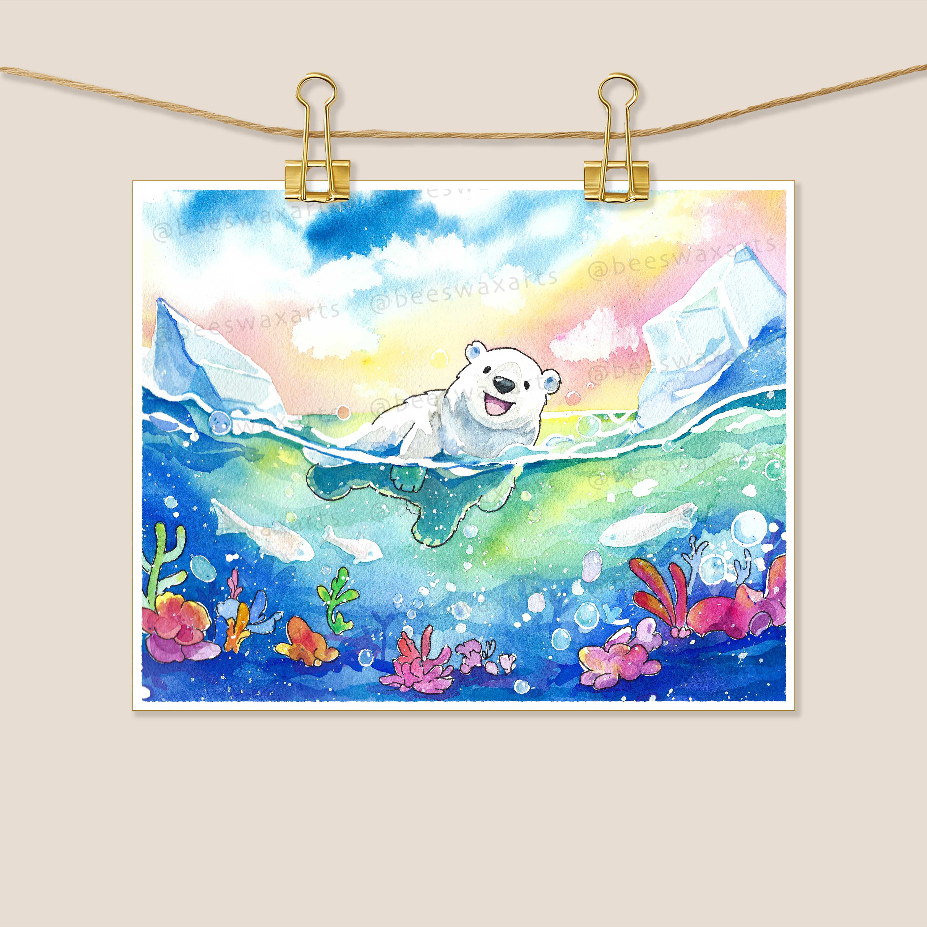 The Polar Bear archival art print by Beeswax Arts Watercolors features a smiling polar bear swimming among icebergs with a vibrant sky and colorful sea plants, and hangs from two gold clips as a unique collectors item.