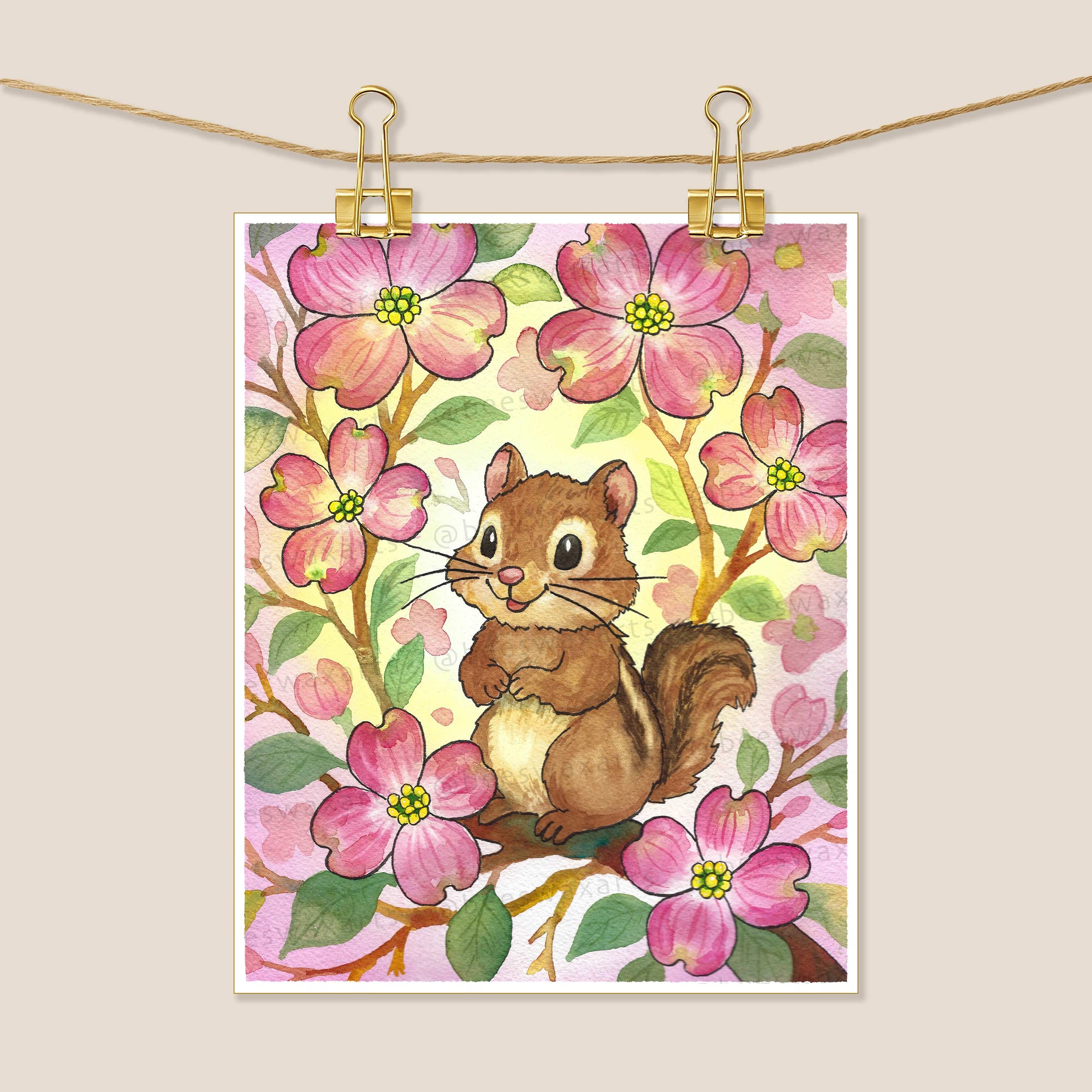 Chipmunk Dogwood by Beeswax Arts Watercolors features a chipmunk on a branch with pink flowers and green leaves, clipped to a string with gold binder clips against a beige background.