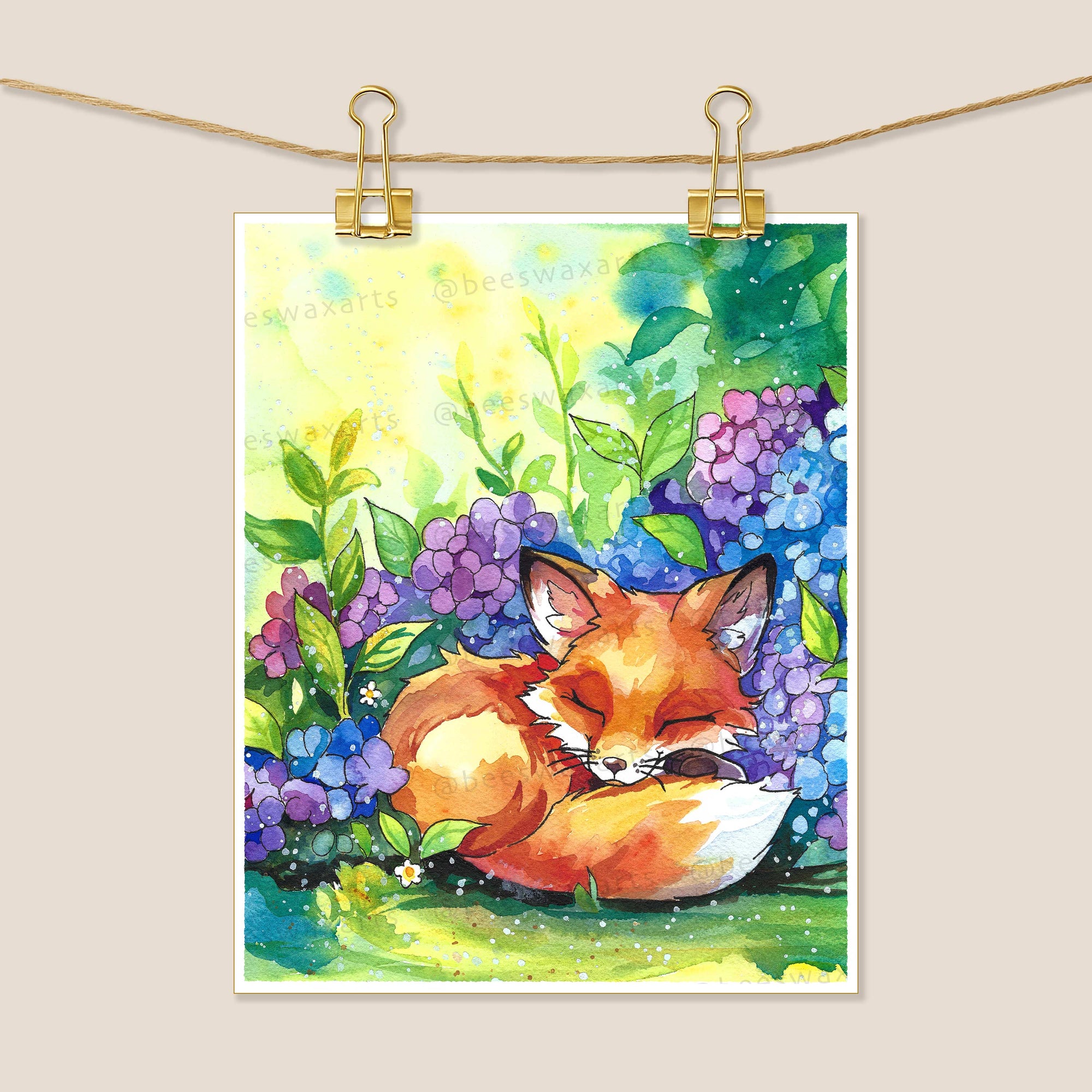 Fox Hydrangeas by Beeswax Arts Watercolors features a sleeping fox among purple and blue hydrangeas with green foliage, clipped on a line against a beige background—a dreamy art print for your space.