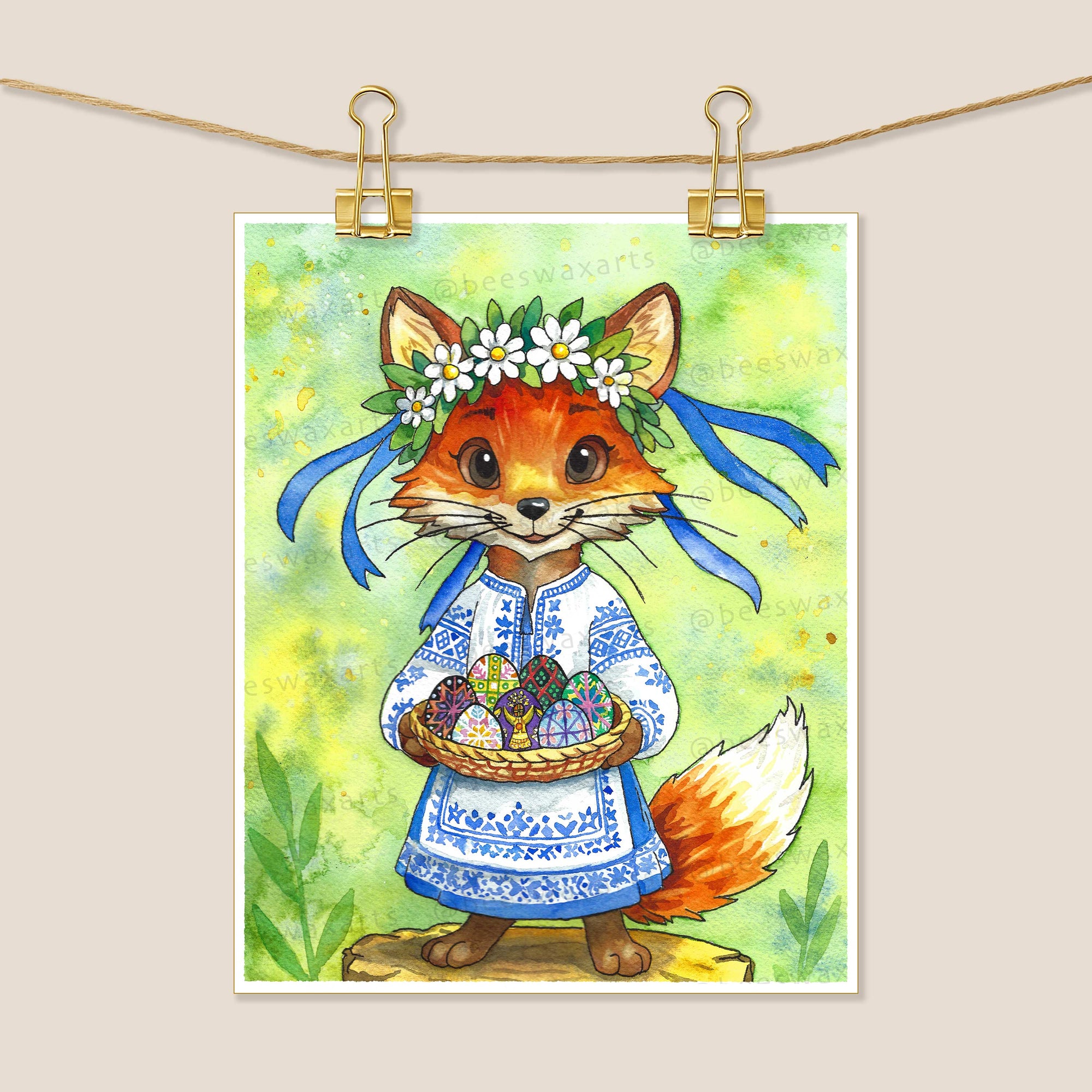 Pysanky Fox by Beeswax Arts Watercolors: an anthropomorphic fox in a blue and white embroidered dress with a flower crown and blue ribbons, holding decorated Easter eggs on a tree stump amid a green nature background—a collectors delight.