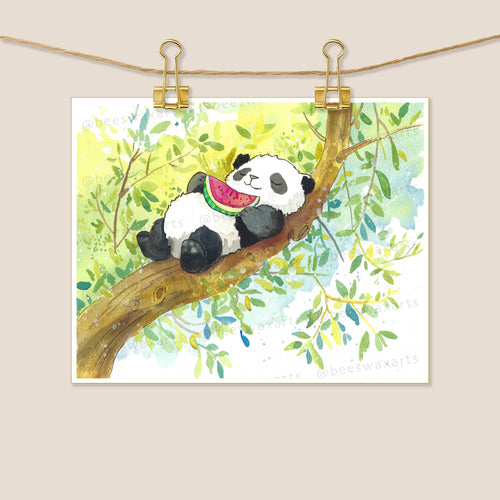 Panda and Watermelon by Beeswax Arts Watercolors is a whimsical watercolor print featuring a panda eating watermelon on a tree branch, surrounded by green leaves, printed on high-quality archival paper and displayed clipped to a line.